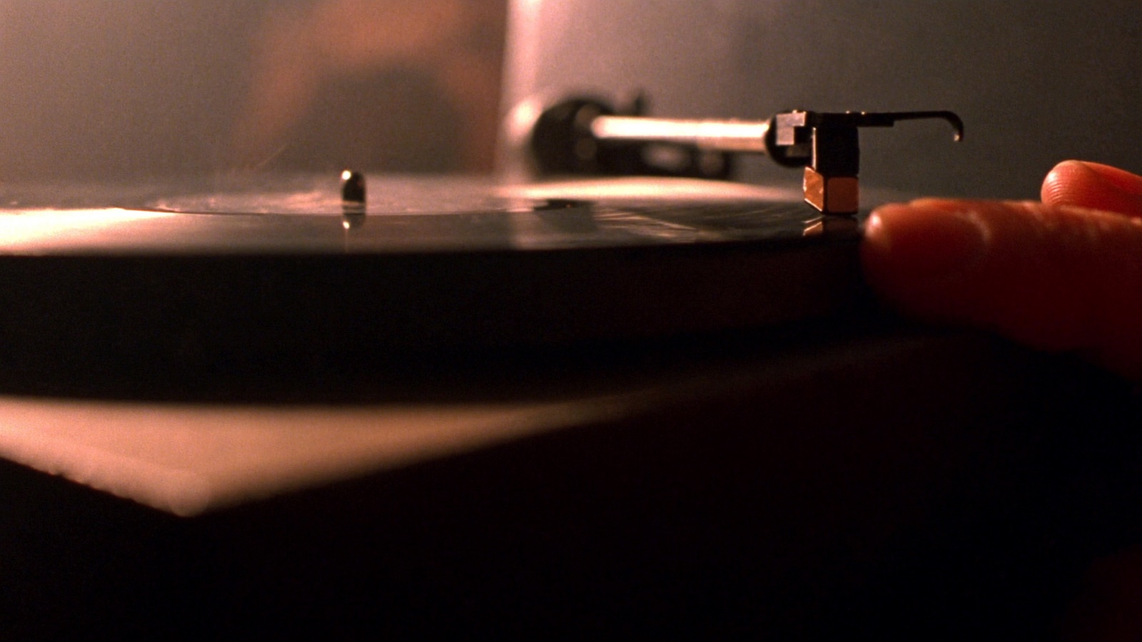 Mão pousando a agulha sobre um disco de vinil girando, em luz quente de abajur